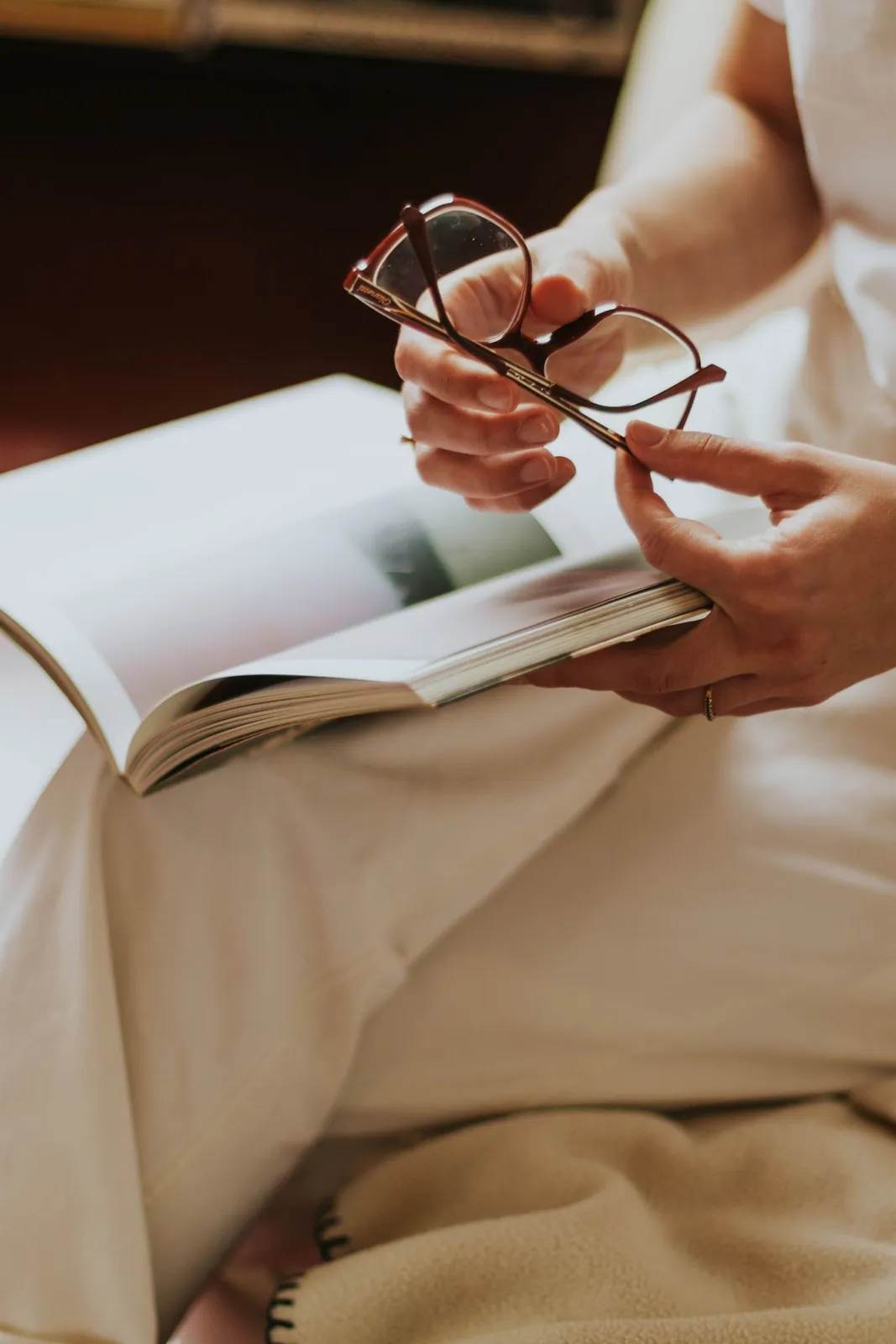 Hände halten eine Brille über einem aufgeschlagenen Buch in warmem Licht